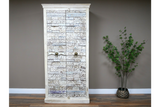 Large white wooden cabinet with intricate carved details and metal ring handles, standing on wooden floor beside green plant.
