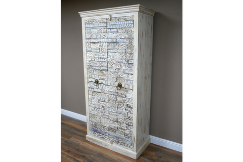 Large wooden cabinet with carved textured whitewashed doors and bronze ring handles, angled view in room.