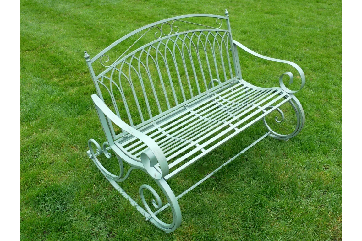Metal garden bench with decorative scroll arms and slatted seat on grass lawn