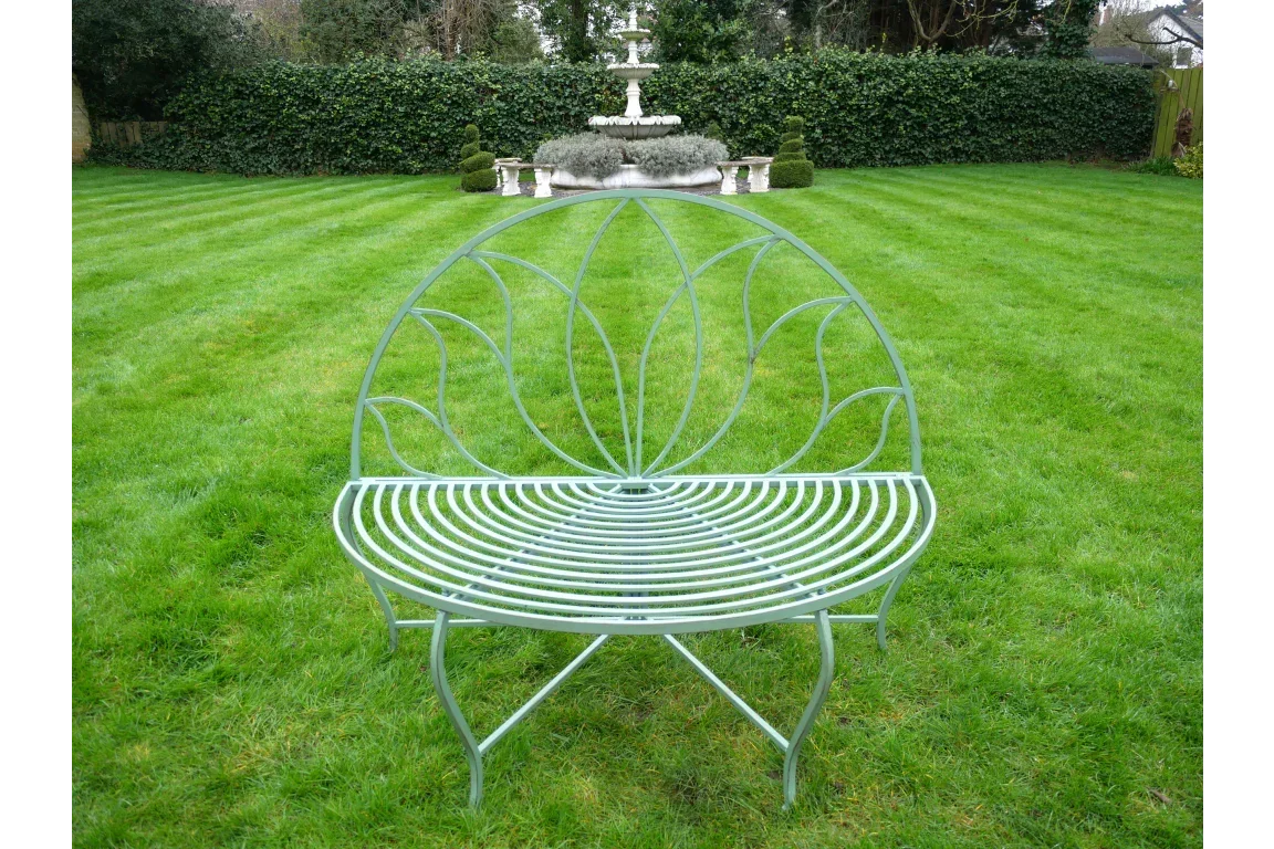 curved metal garden bench with leaf pattern backrest on lawn, fountain in background