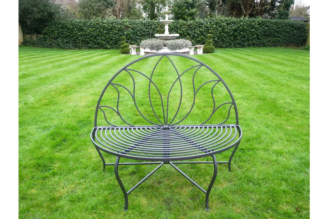 Black metal garden bench with decorative backrest on lawn, fountain visible in background
