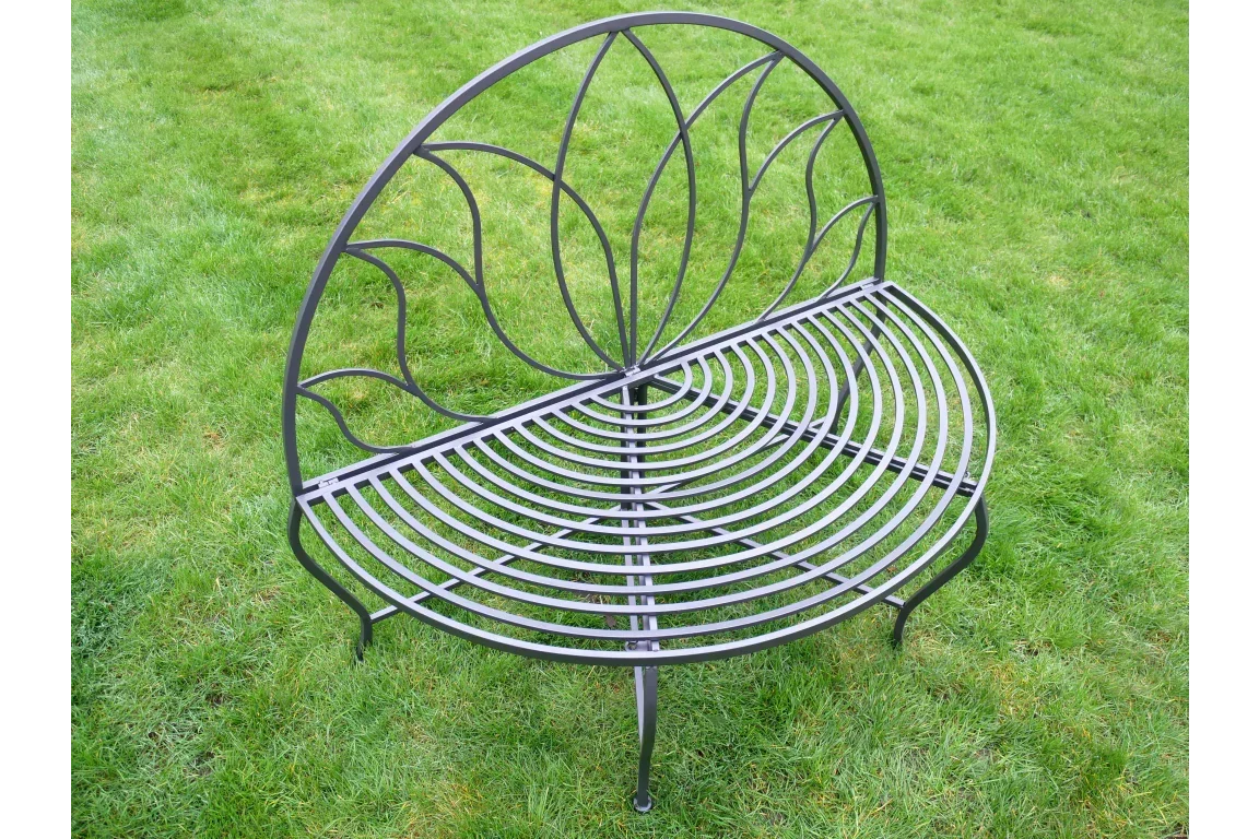 Black metal garden bench with curved slatted seat and decorative leaf backrest on grass
