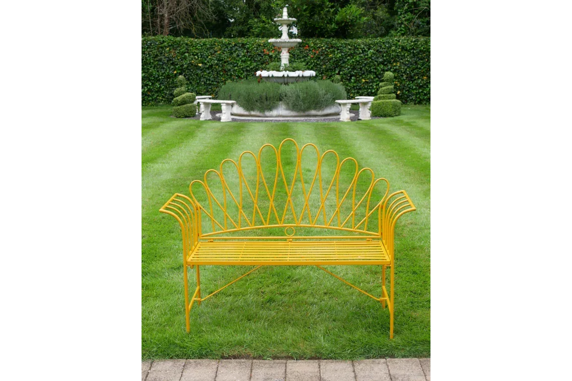 Yellow metal garden bench with decorative backrest on lawn