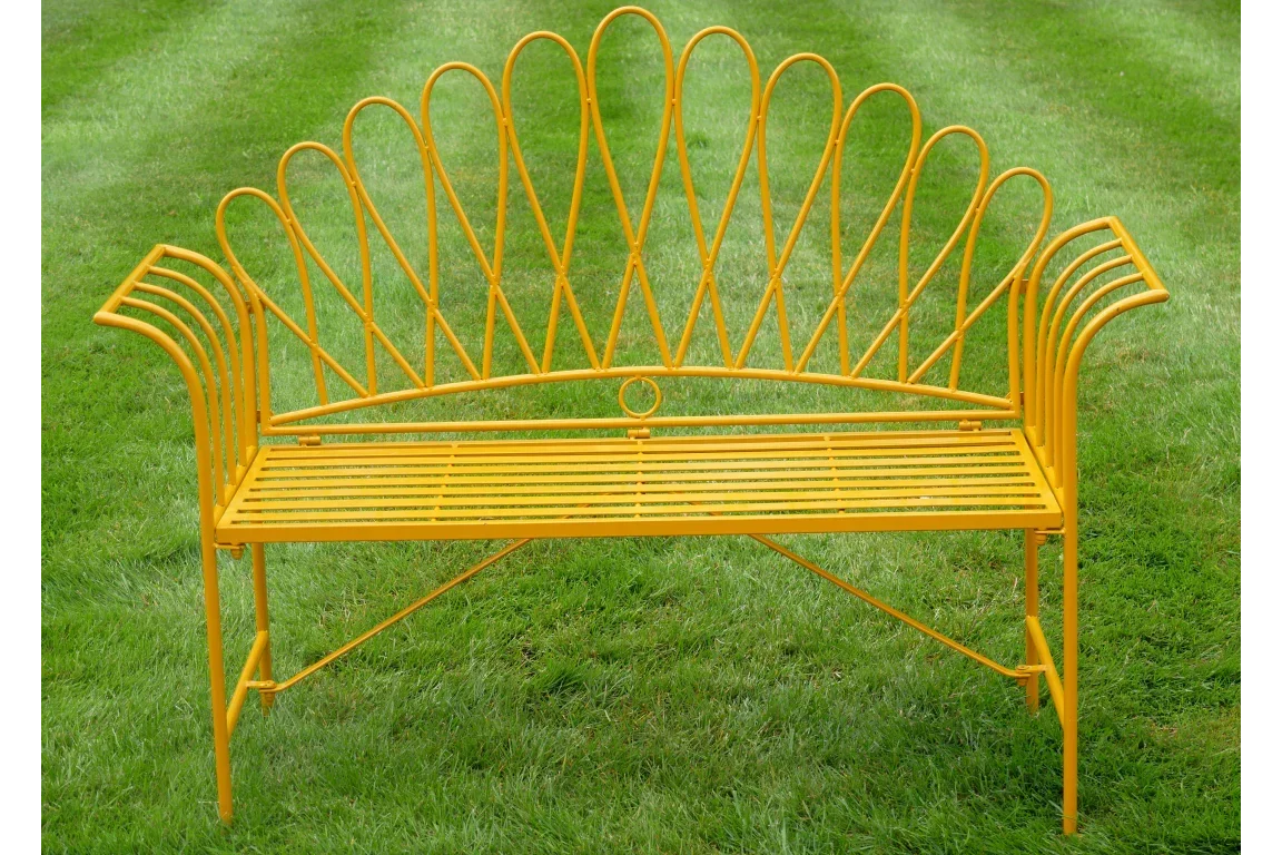 Yellow metal garden bench with decorative backrest on green grass