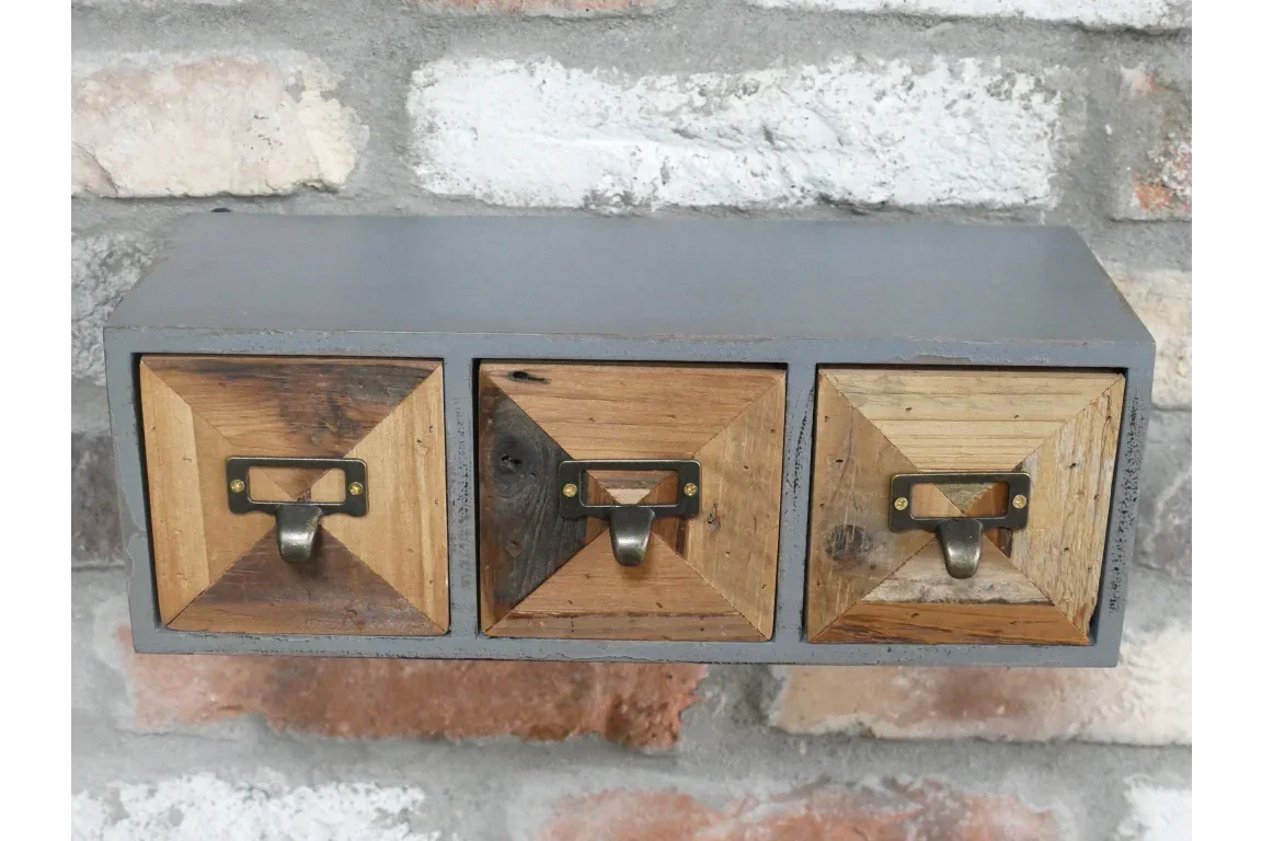 Three drawer rustic wood wall organiser with metal handles against brick wall