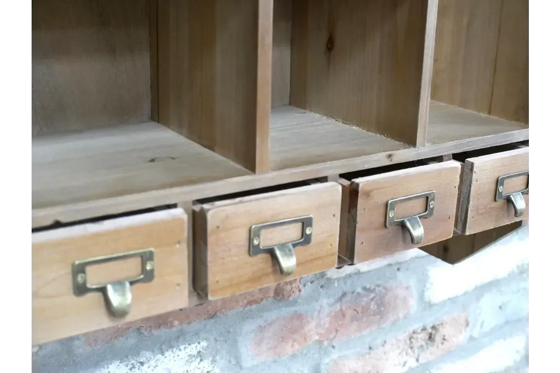 Wooden storage unit with three small drawers and brass handles, mounted on a brick wall