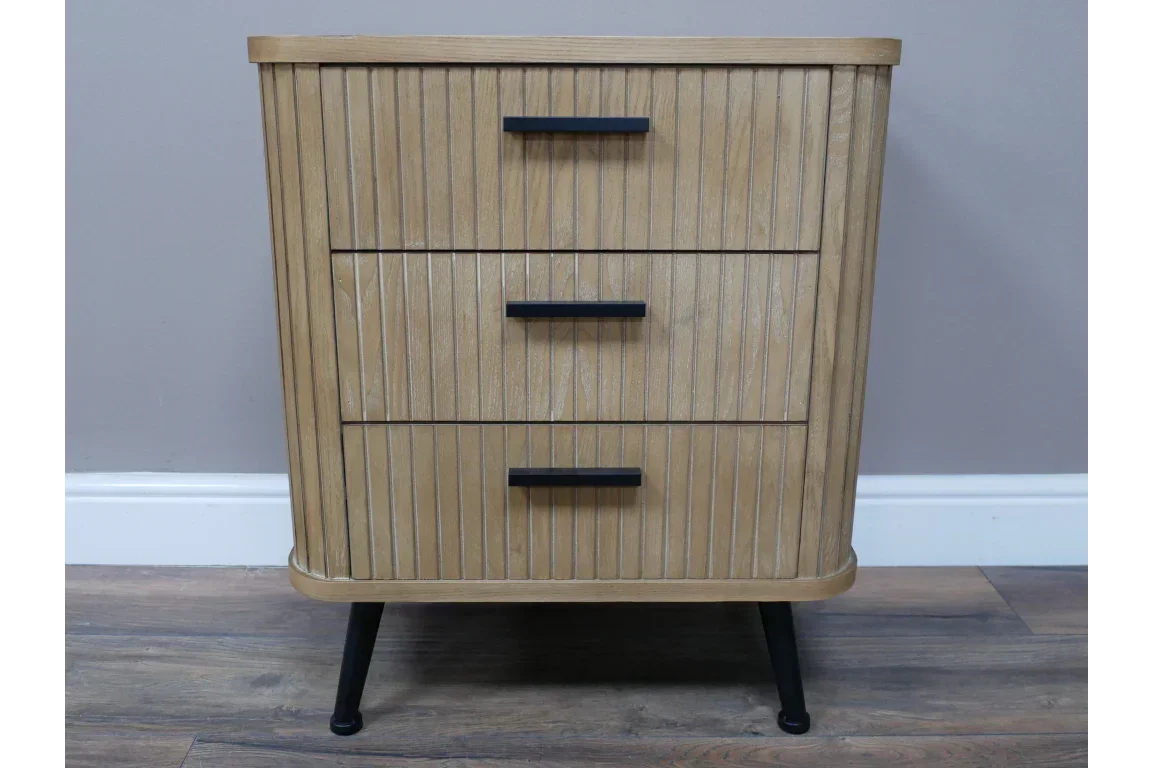 Oak bedside table with three drawers, black handles, and ribbed wood detail on wooden floor