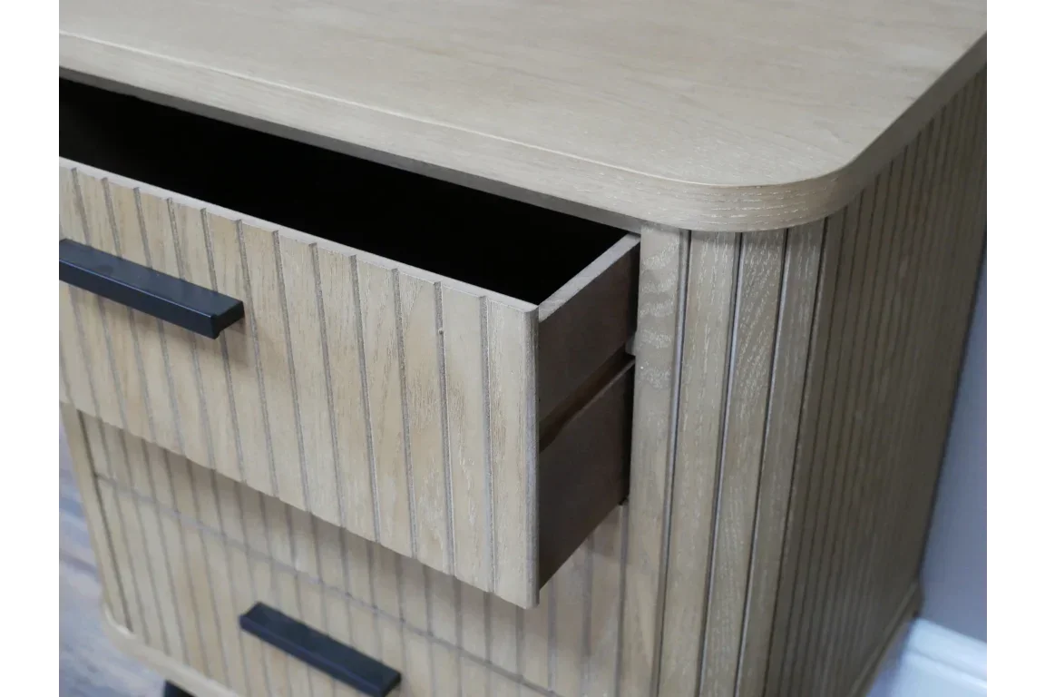 Wooden chest of drawers with vertical grooves and black handles, top drawer open