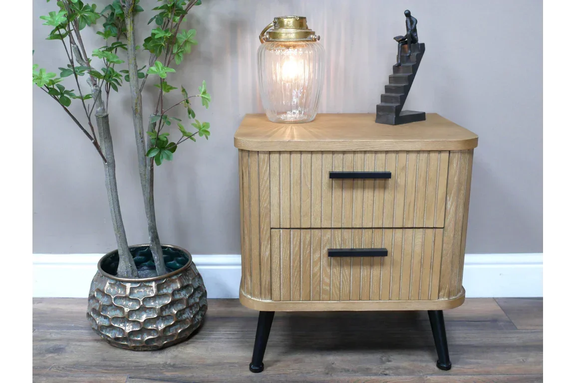 Oak bedside table with two drawers, black handles, lamp and sculpture on top, indoor setting