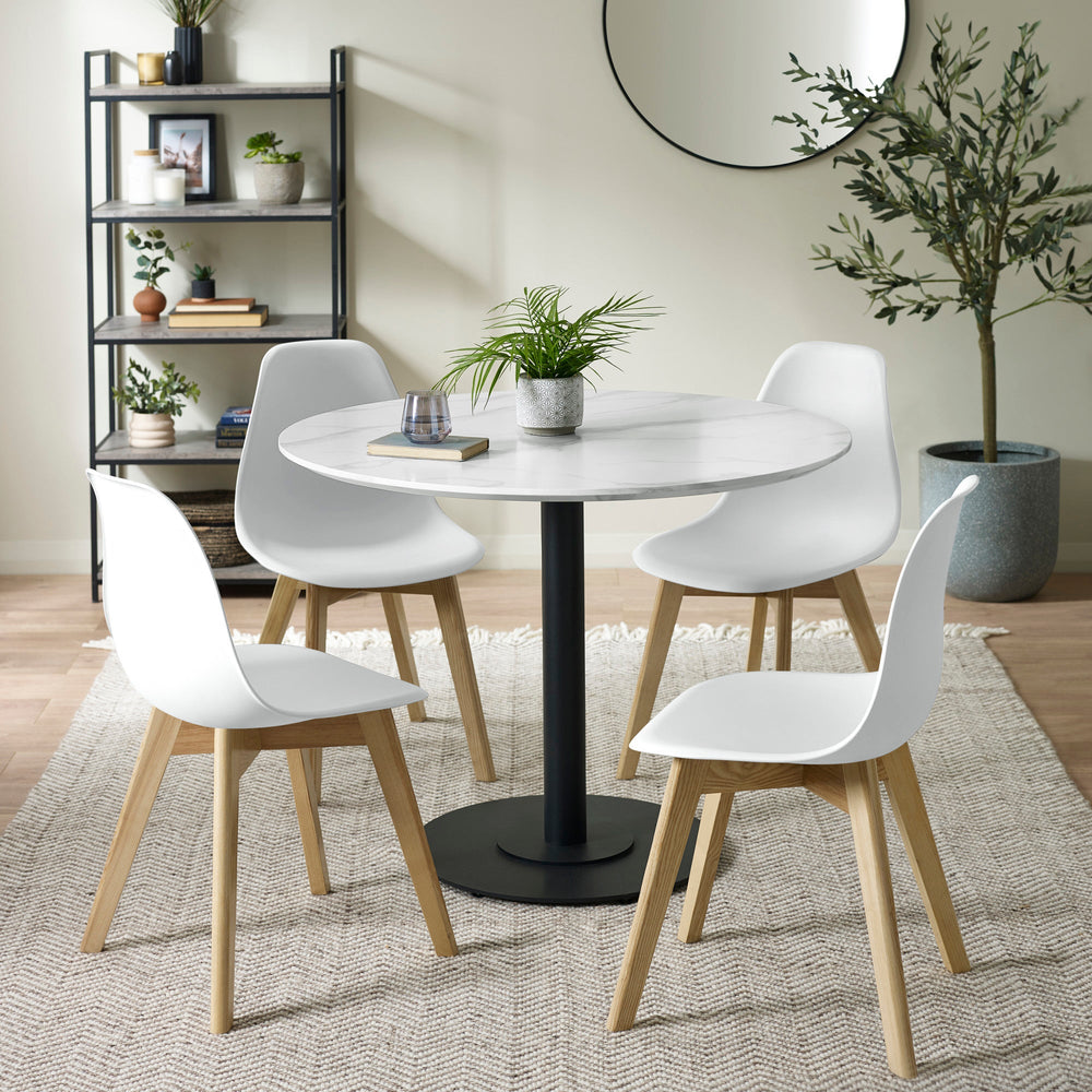 Dining room setting with four white chairs and round white marble table on woven rug