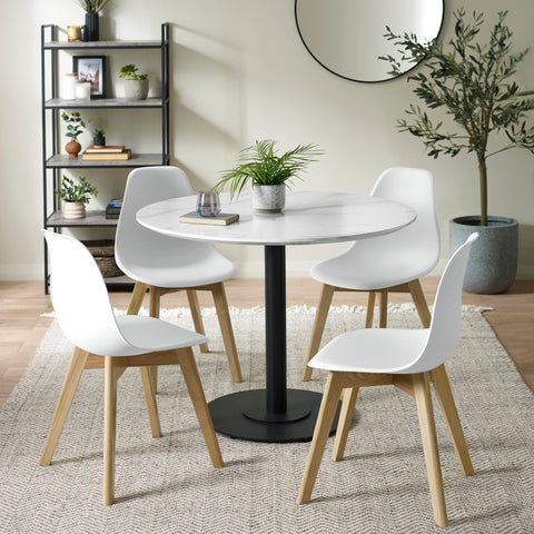 Dining room setting with four white chairs and round white marble table on woven rug