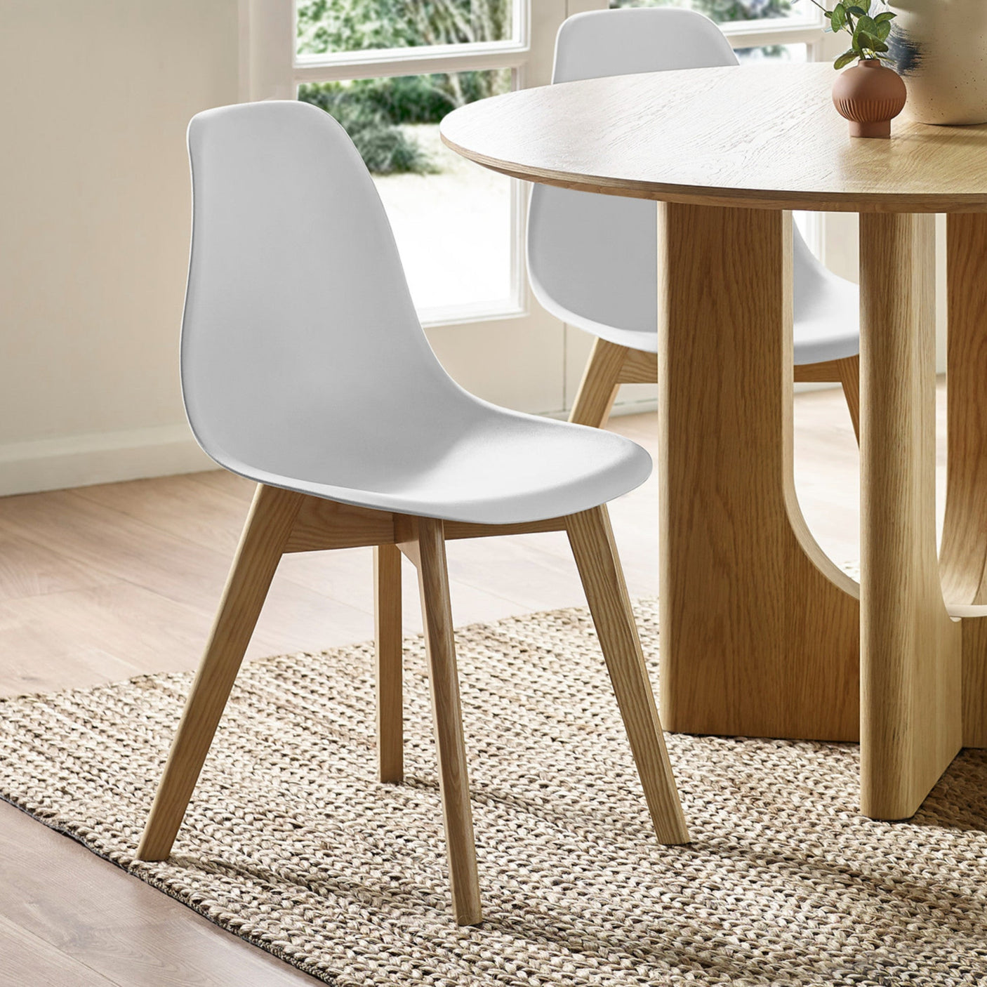 White dining chair with curved plastic seat and wooden legs beside oak dining table indoors