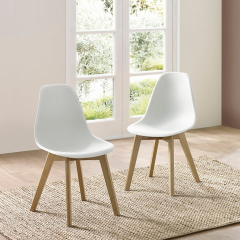 Two white dining chairs with wooden legs on woven rug next to window with green outdoor view