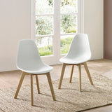Two white dining chairs with wooden legs on woven rug next to window with green outdoor view