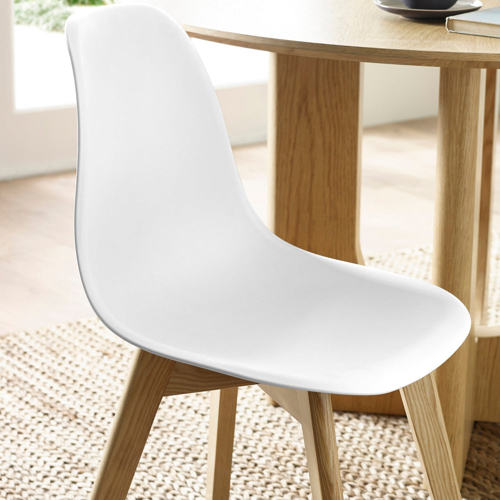 Close-up of white molded plastic seat and wooden legs on natural fiber rug next to oak dining table