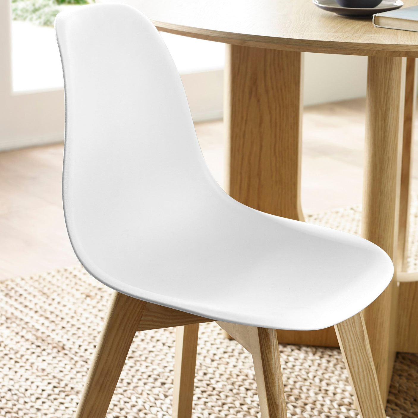 Close-up of white molded plastic seat and wooden legs on natural fiber rug next to oak dining table