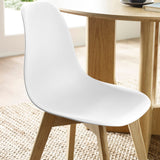 Close-up of white molded plastic seat and wooden legs on natural fiber rug next to oak dining table