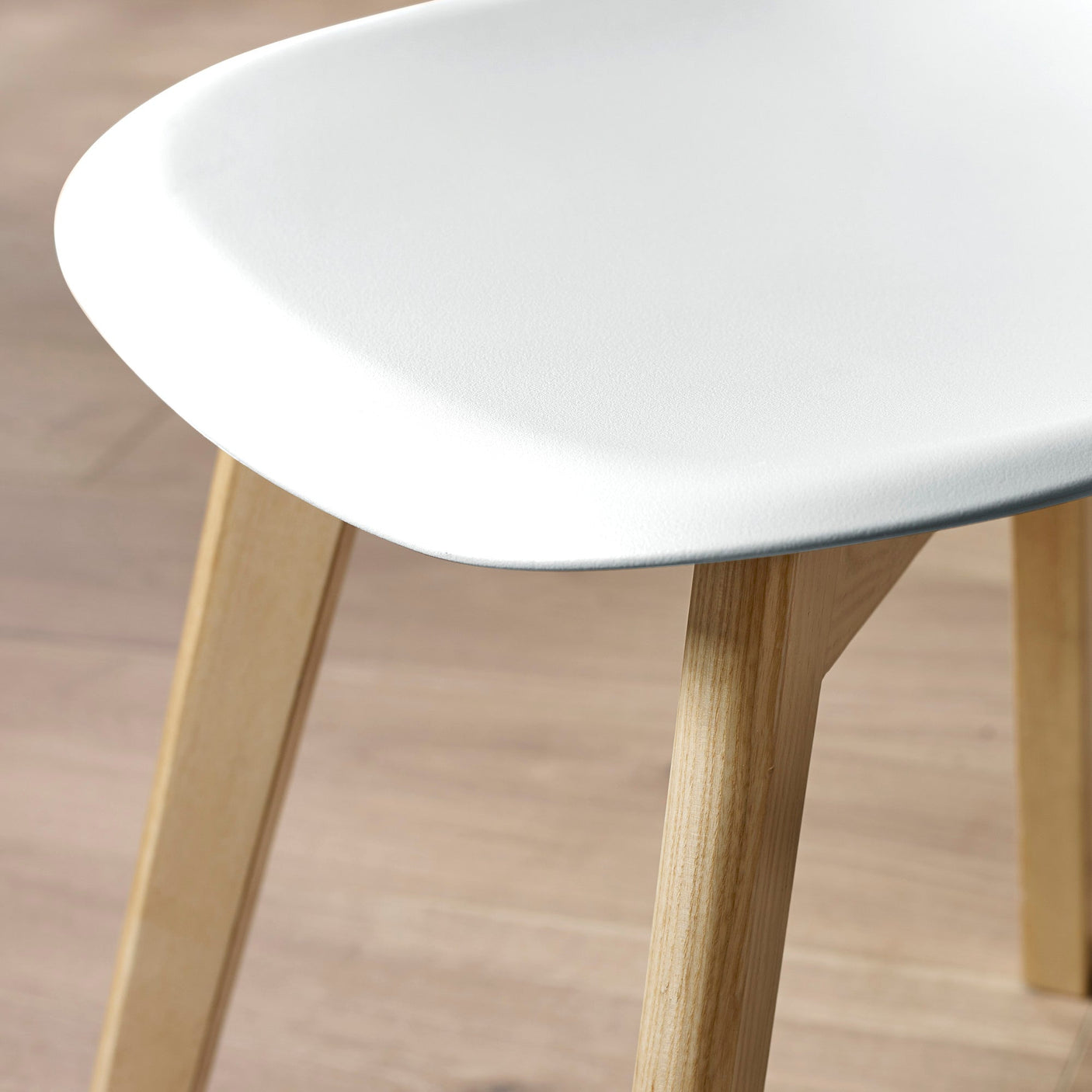Close-up of white plastic seat and light wood legs on light wood floor