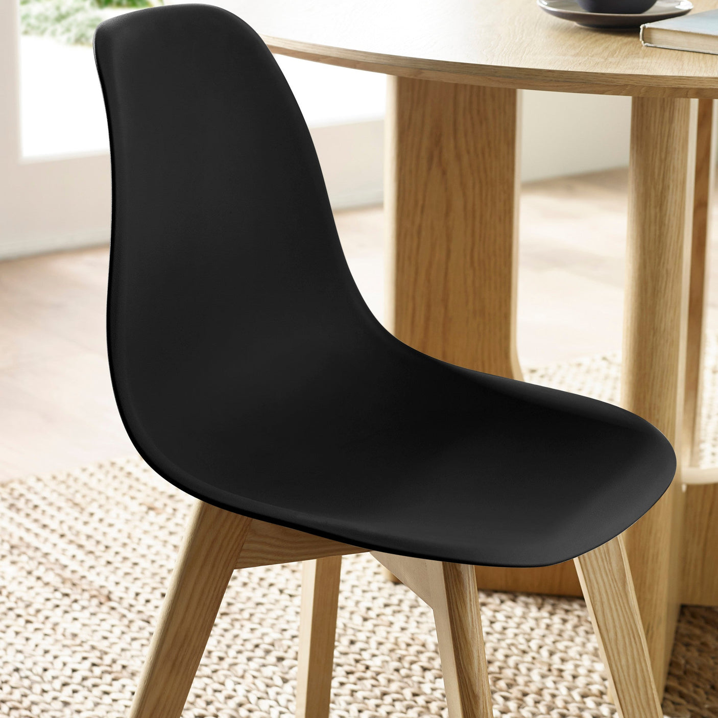 Close-up of matte black seat back and top edge with natural wood legs under light wood table on rug.