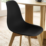 Close-up of matte black seat back and top edge with natural wood legs under light wood table on rug.