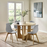 Four grey dining chairs with wooden legs around a round wooden table in a bright room with glass doors and wall art