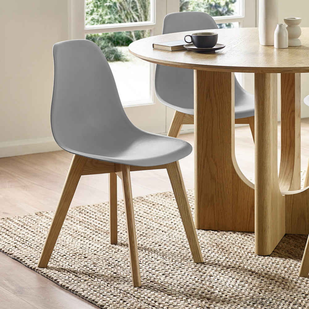 Light grey plastic chair with light wooden legs on beige jute rug next to round light oak table in room