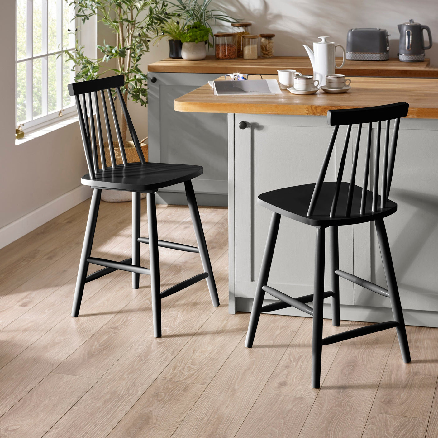 Two black wooden bar stools with spindle backs next to a kitchen island and window in natural light.