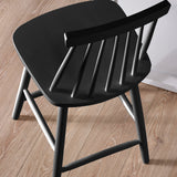 Close-up of black wooden bar stool back showing smooth finish and spindle detail on wood floor.