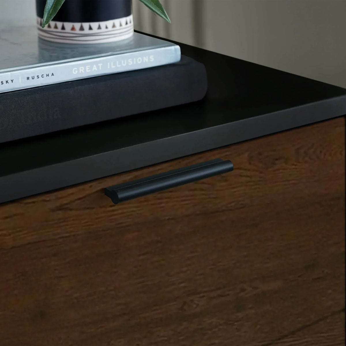 Walnut bedside table with black top, modern handle, and books stacked on the surface