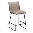 A modern counter stool with a light taupe-beige padded seat and backrest featuring vertical channel tufting, supported by a black metal frame with a footrest.