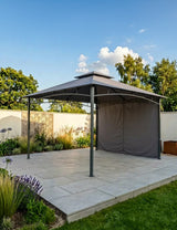 Grey metal garden gazebo with canopy and side panel on paved patio in landscaped yard