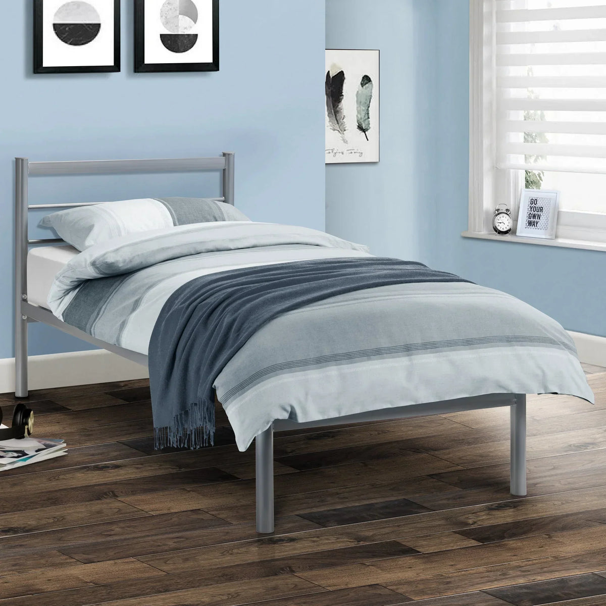 Metal single bed with grey frame and blue bedding in a modern bedroom with wood flooring