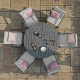 Round grey outdoor dining set with six cushioned chairs and pink pillows on stone patio