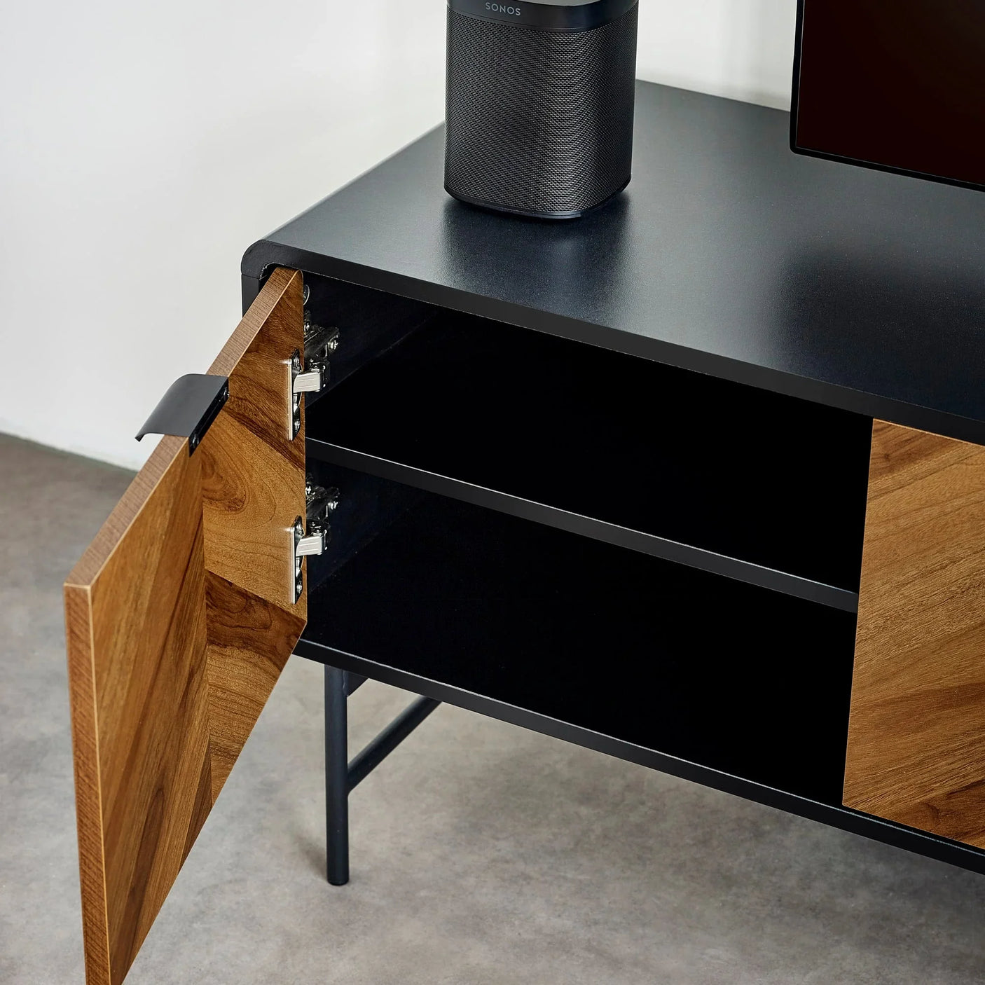 Black and wood TV unit with open cabinet door, two shelves and metal legs on grey floor