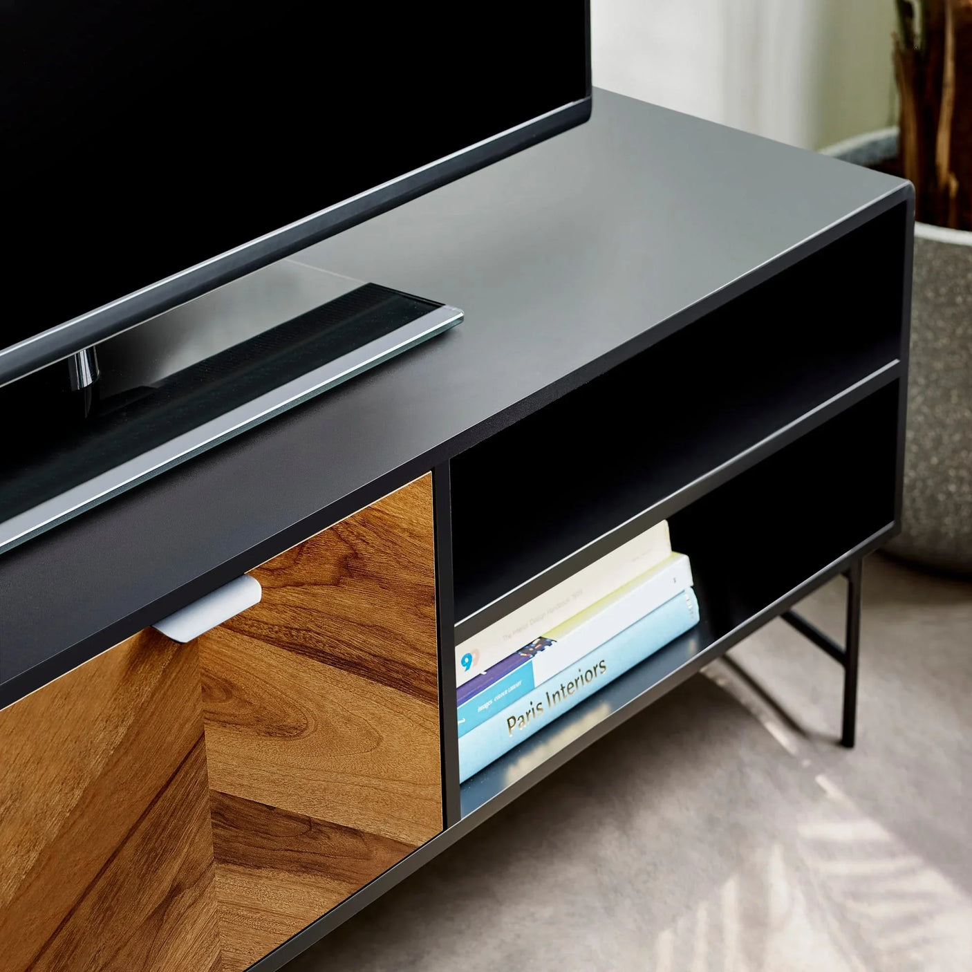 Modern black TV unit with wood front, open shelf, and books styled under television