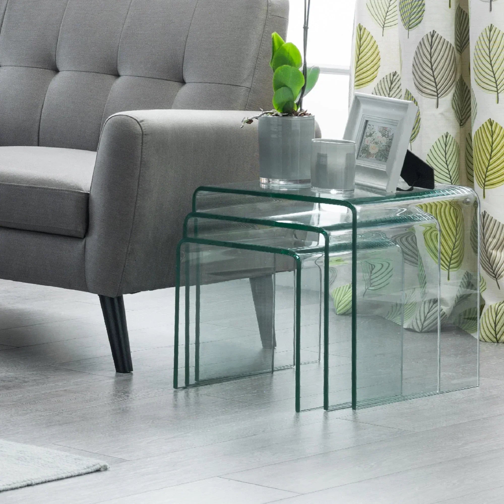 Glass nest of tables beside grey sofa with plant and photo frame, modern living room