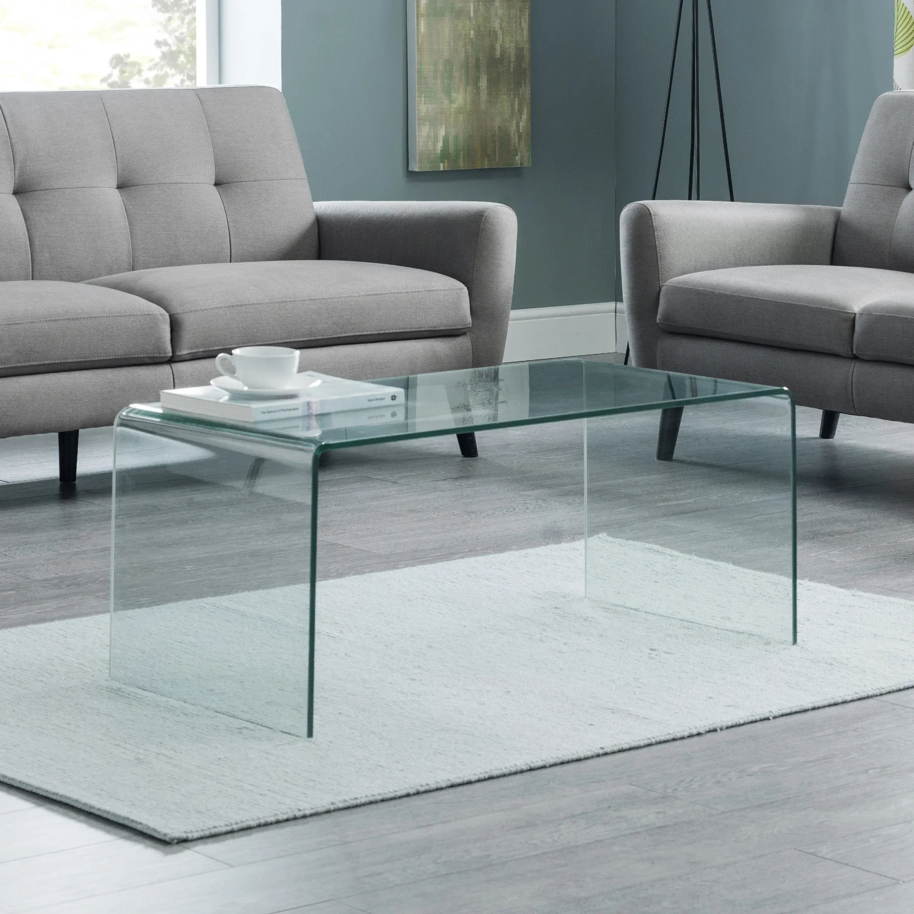 Glass coffee table with curved edges on grey rug between two grey sofas in modern living room