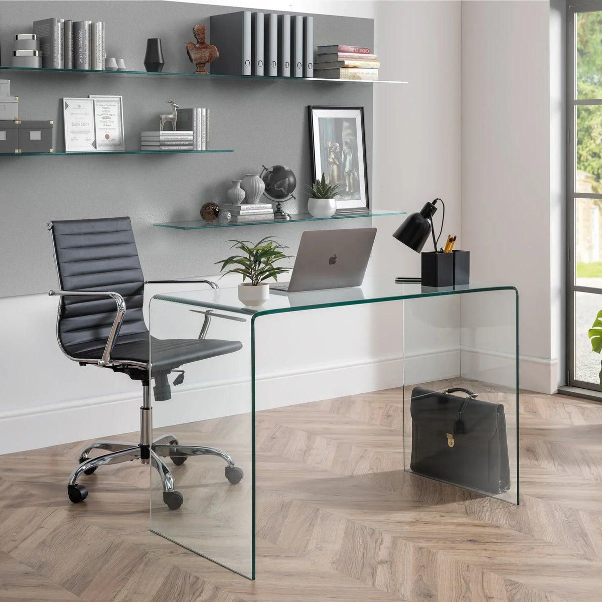 Curved glass desk with laptop, lamp, and office chair in modern home office setting