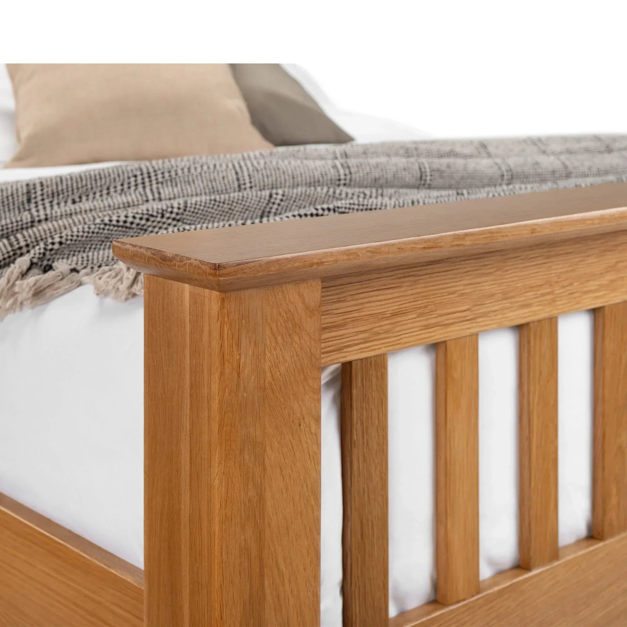 Close-up of oak bed frame footboard with slatted design, bedding and throw visible