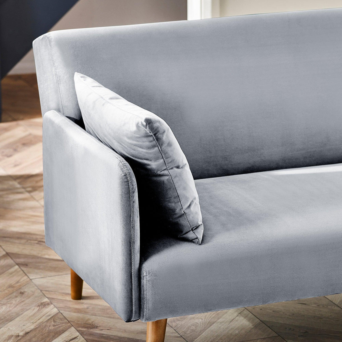 Closeup of grey sofa bed armrest and cushion with wooden legs on parquet floor