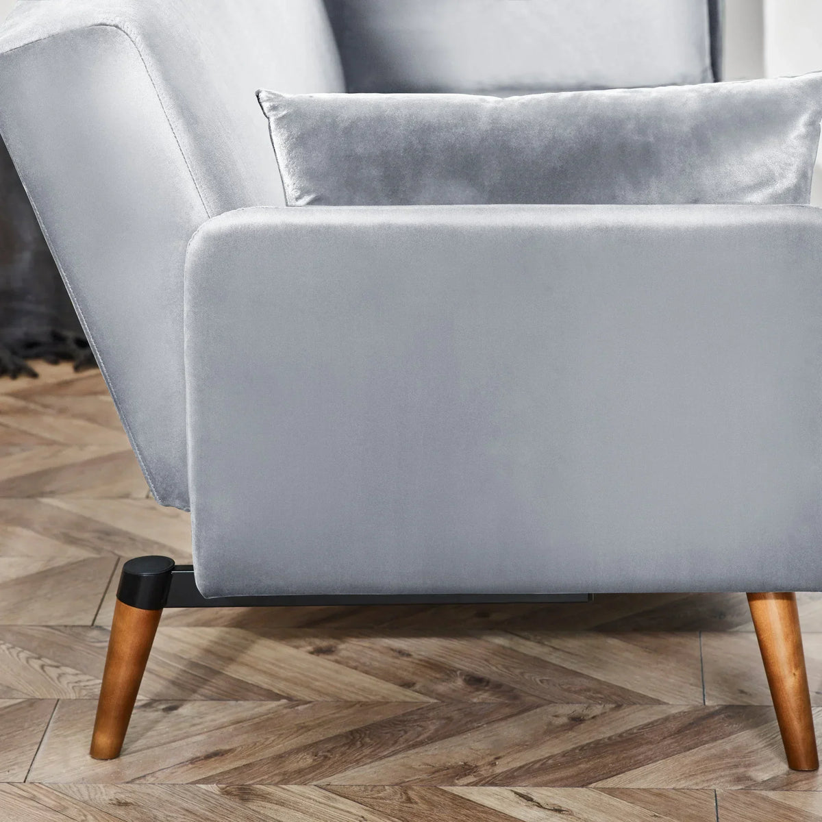 Grey sofa bed corner with wooden legs and matching cushion on herringbone wood floor