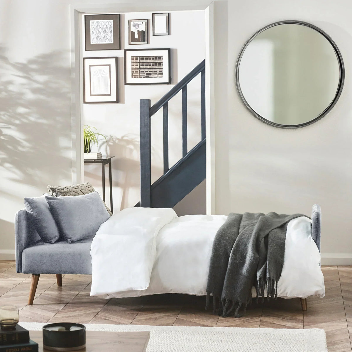 Grey sofa bed with wooden legs in modern living room, dressed with white bedding and throw