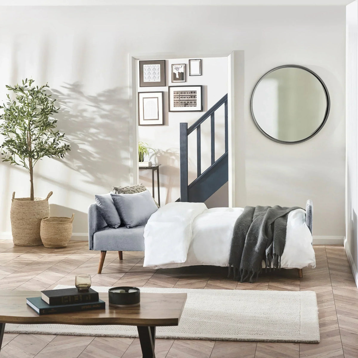 Grey sofa bed in living room, styled as bed with white duvet and dark grey throw