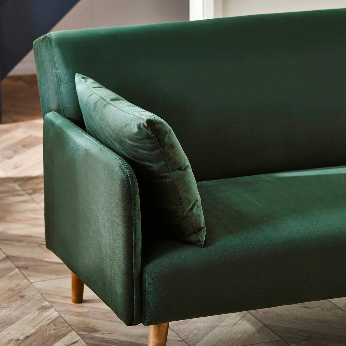 Green velvet sofa bed armrest and cushion with wooden legs on parquet floor
