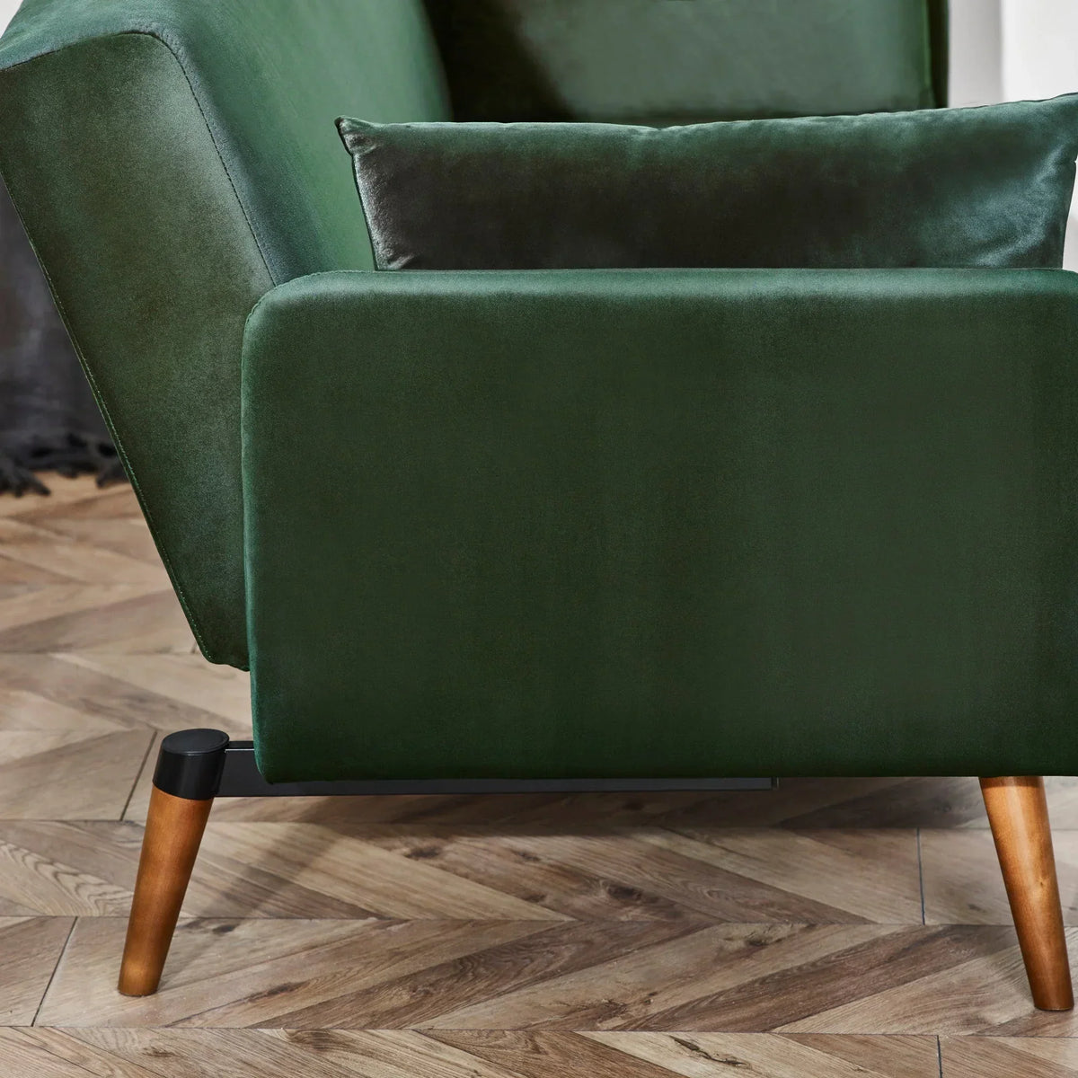 Green sofa bed detail with velvet upholstery and wooden legs on herringbone floor
