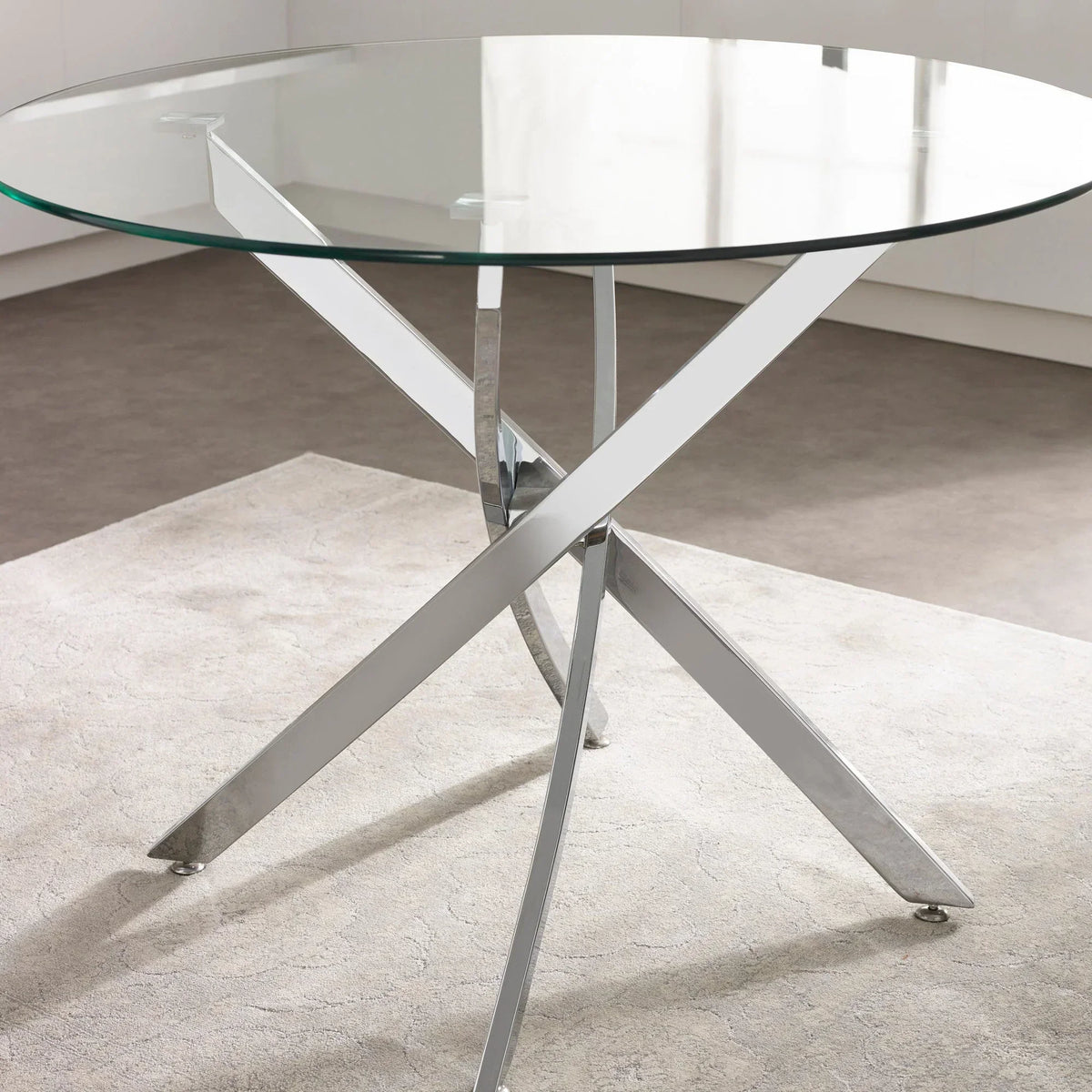Round glass dining table with crossed chrome legs on a light rug