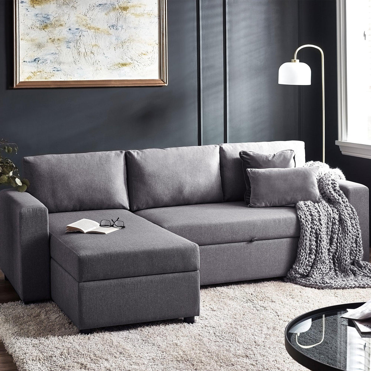 Grey sofabed with storage, chaise lounge, and cushions in modern living room setting