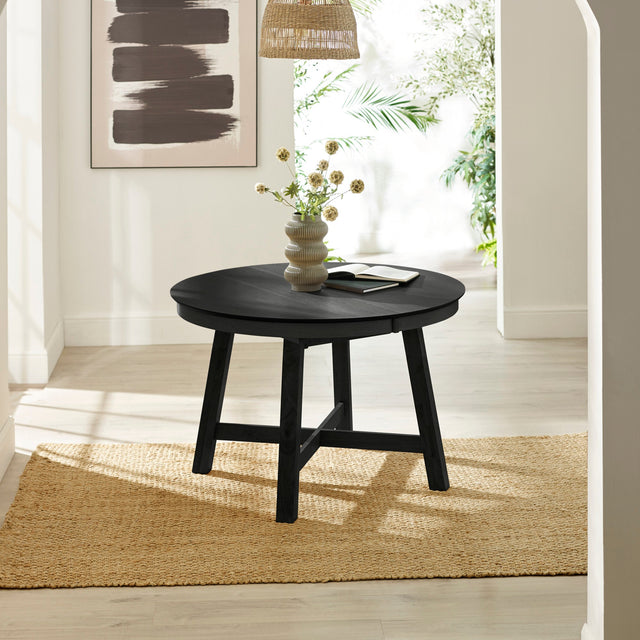 Black round wooden dining table with four tapered legs on woven rug in bright room