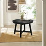 Black round wooden dining table with four tapered legs on woven rug in bright room