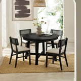 Round black wood dining table with four black cane-back chairs on beige rug, with vase and books in bright room